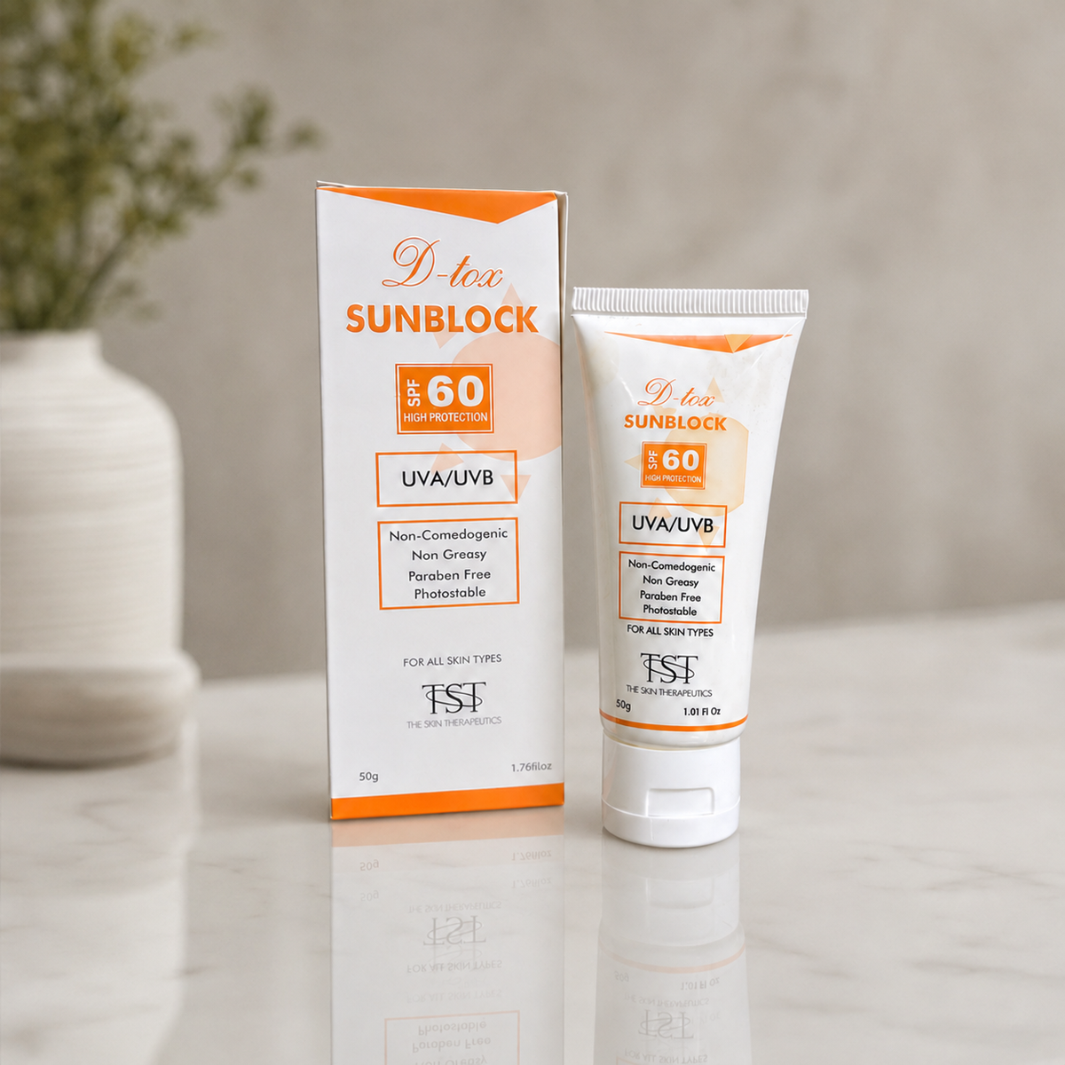 A tube and box of D-tee SUNBLOCK SPF 60 sunscreen are displayed on a light marble surface with a soft-focus background featuring a white vase with greenery.